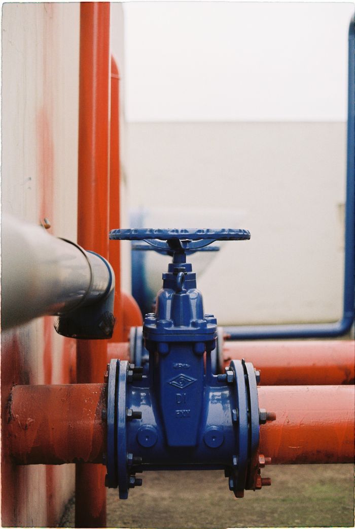 hero-01 Close-up of a blue gate valve on red pipes, showcasing industrial plumbing.