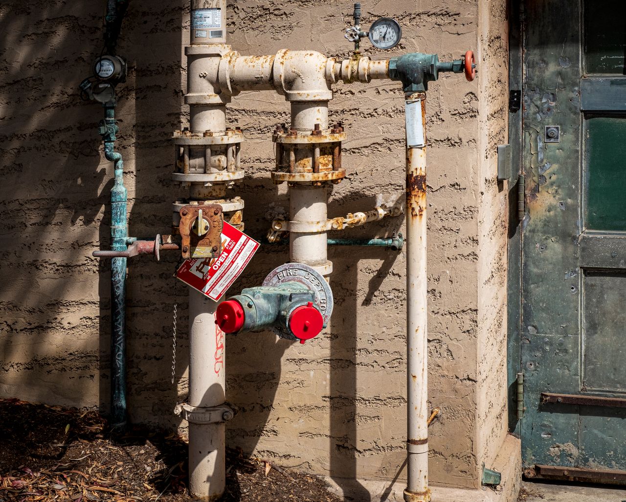 services-05 Rusty outdoor plumbing pipes with pressure gauges and warning signs on a wall.