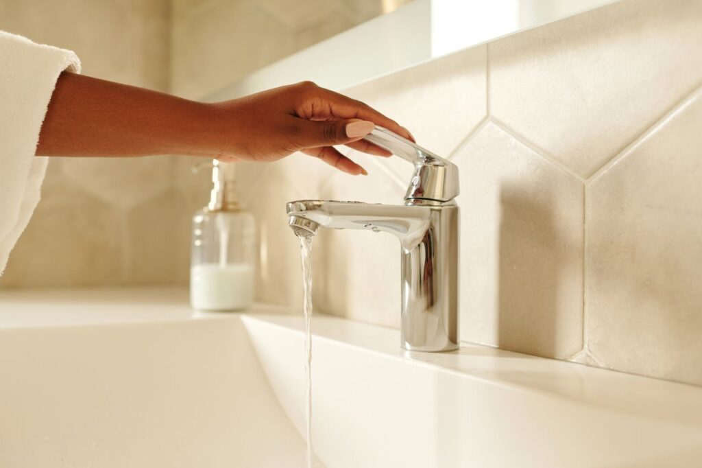 Mastering the First Impression: Your intriguing post title goes here A close-up shot of a hand operating a chrome bathroom faucet with water flowing in a modern bathroom setting.