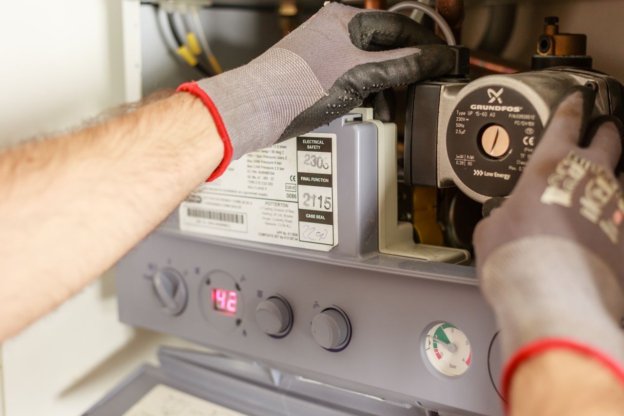 hero-02 Close-up of hands adjusting a boiler system with precise instrumentation, showing maintenance work.